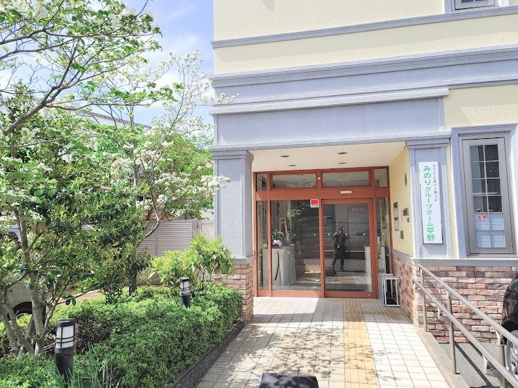 ２階建ての建物で、クリーム色の壁にグレーのアクセントがあり、下部はレンガ調である。玄関前にスロープと手すりが設置されている。
