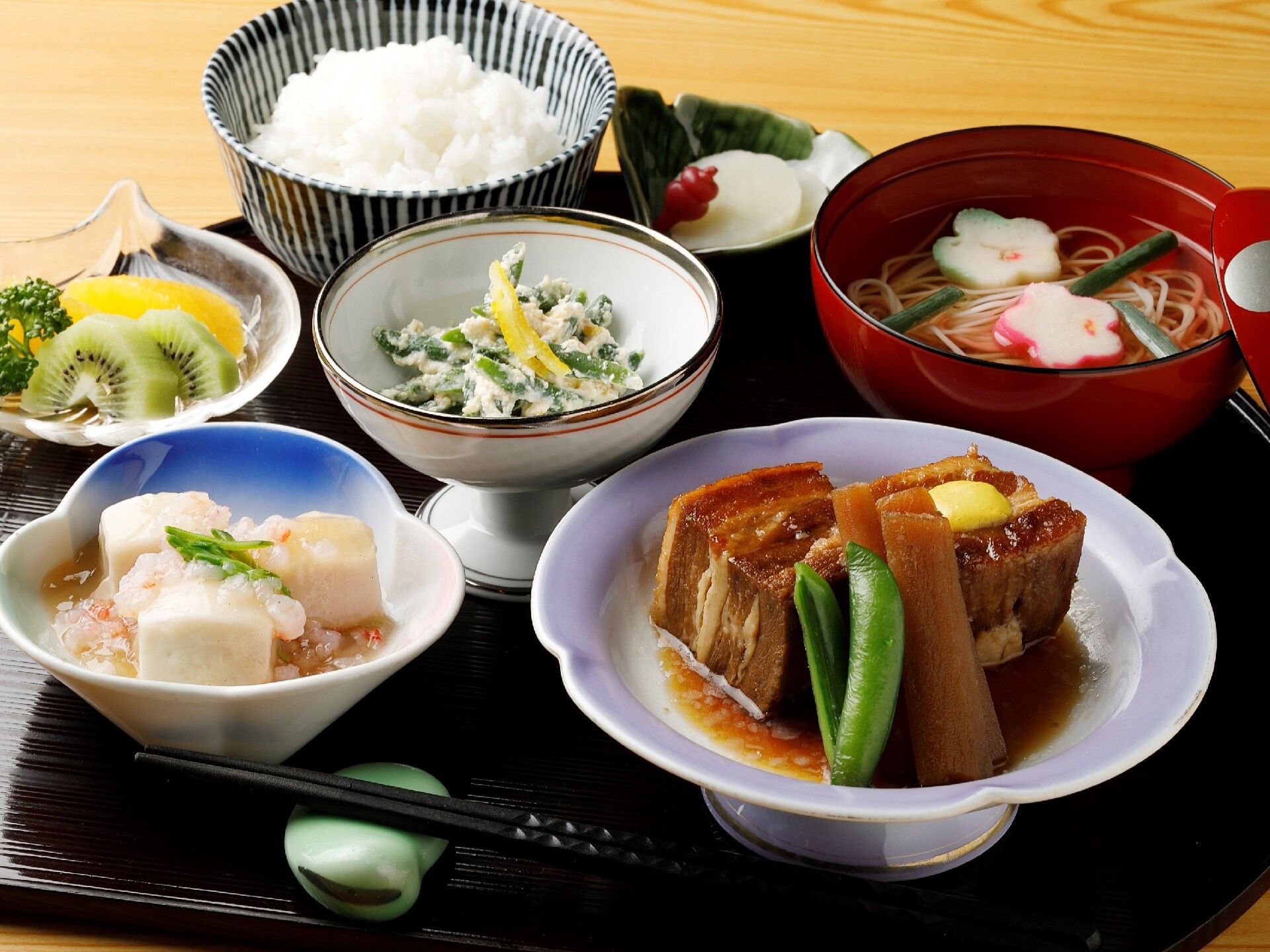 豚の角煮、高野豆腐の煮物、そうめん汁など５種のおかずとフルーツ、ご飯が付いた献立