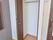 括り付けのクローゼットが部屋にはついていて、扉が開いている。ハンガーをかけるポールがついている。その隣にハンドルのついたドアが見える。