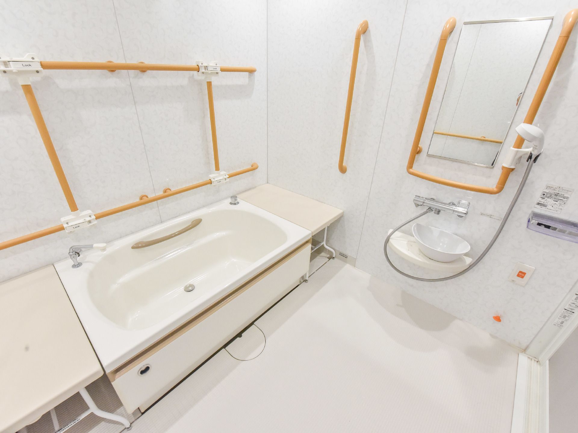 手すりが壁についたお風呂場で、白いバスタブが設置してある。ベンチがあり、段差をなくし浴槽に入りやすくなっている。
