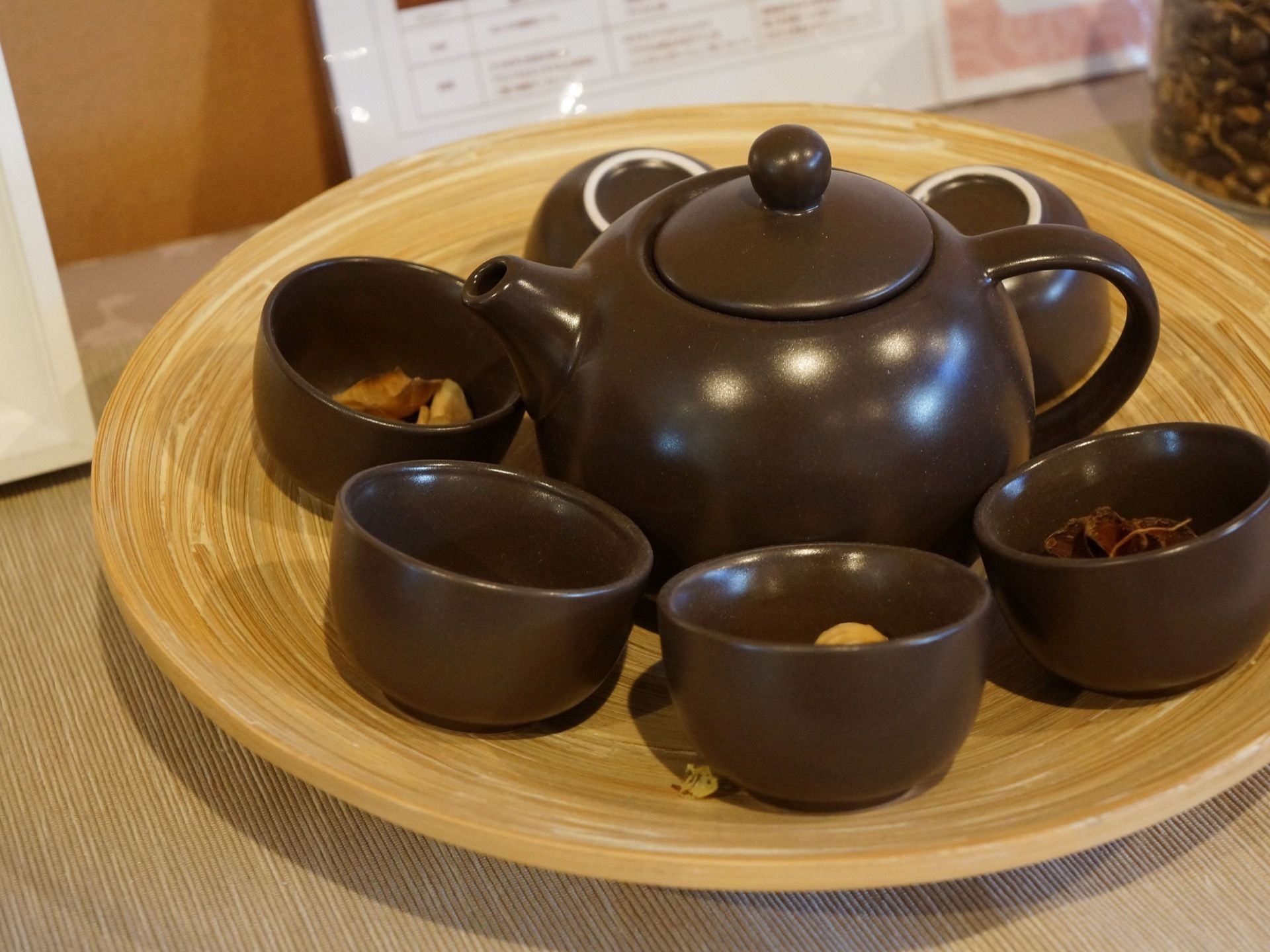 丸い木製の大皿の上に、急須が置かれている。その周りを囲むように、６個の湯飲みがある。４つは上向きになっており、中に茶葉が入っている。