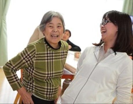 明るいリビングルームで立ったまま笑顔を向ける入居者と介護スタッフ