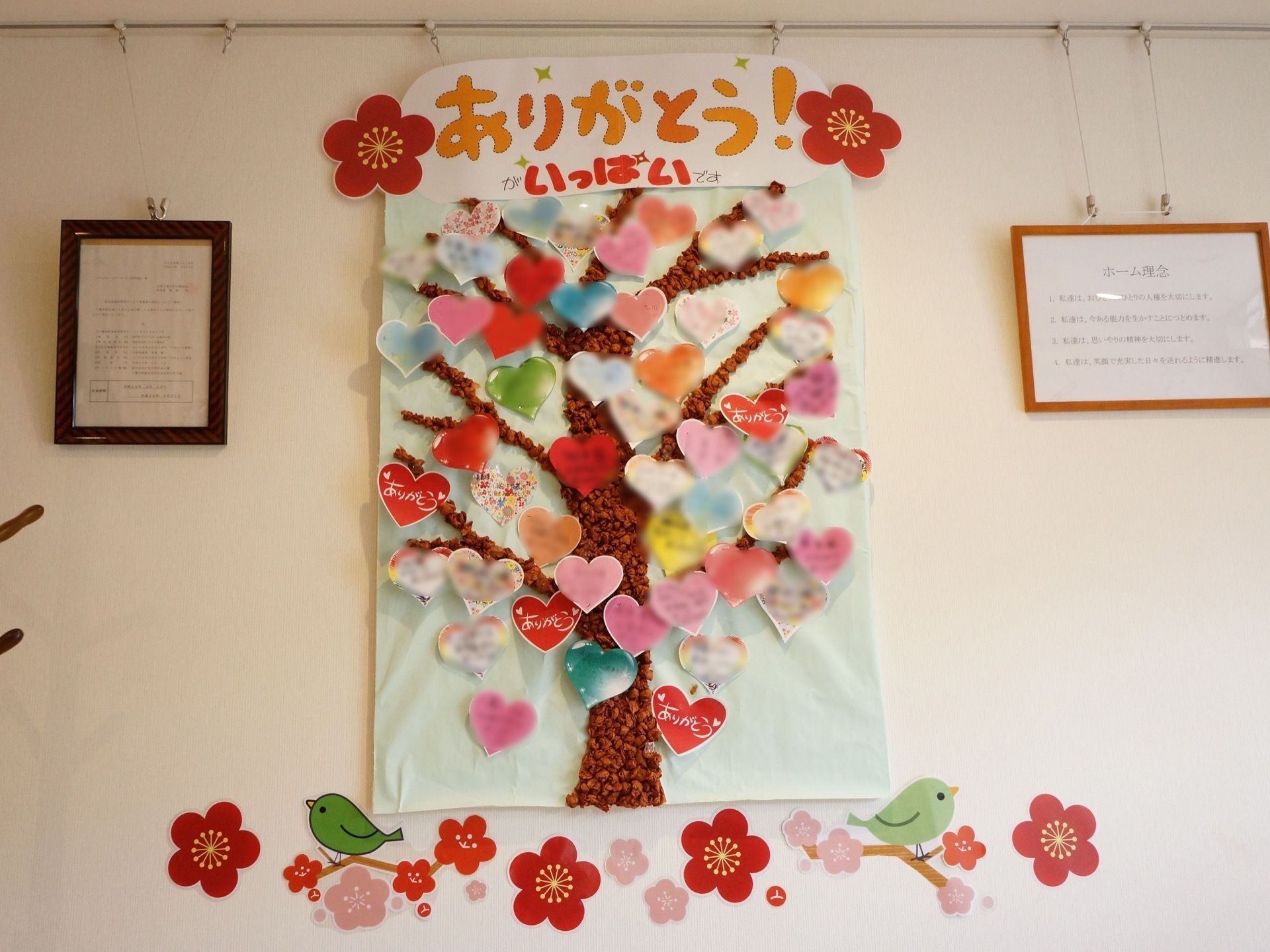 壁には、それぞれの入居者様が書いたハート型の色紙に木の絵とともに花びらとして飾られており、思いで作りの一環である。
