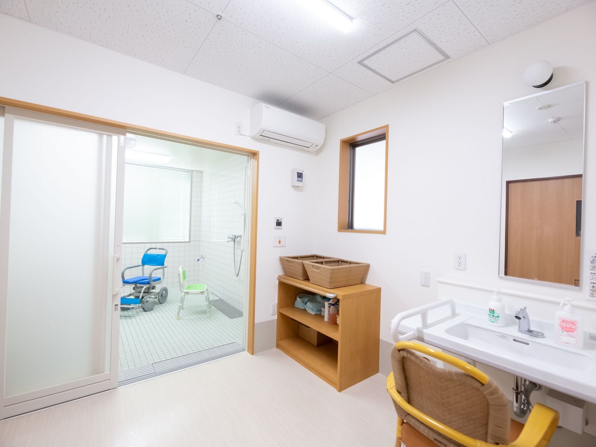 浴室前にある脱衣所の様子である。白色を基調とした明るく清潔な室内で、壁沿いに棚や脱衣かごが置かれており、エアコンも完備されている。