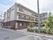 施設は3階建ての建物である。左側には道路が通っており、入り口の右側にはシルバーの看板、左側にはのぼりが立っている。