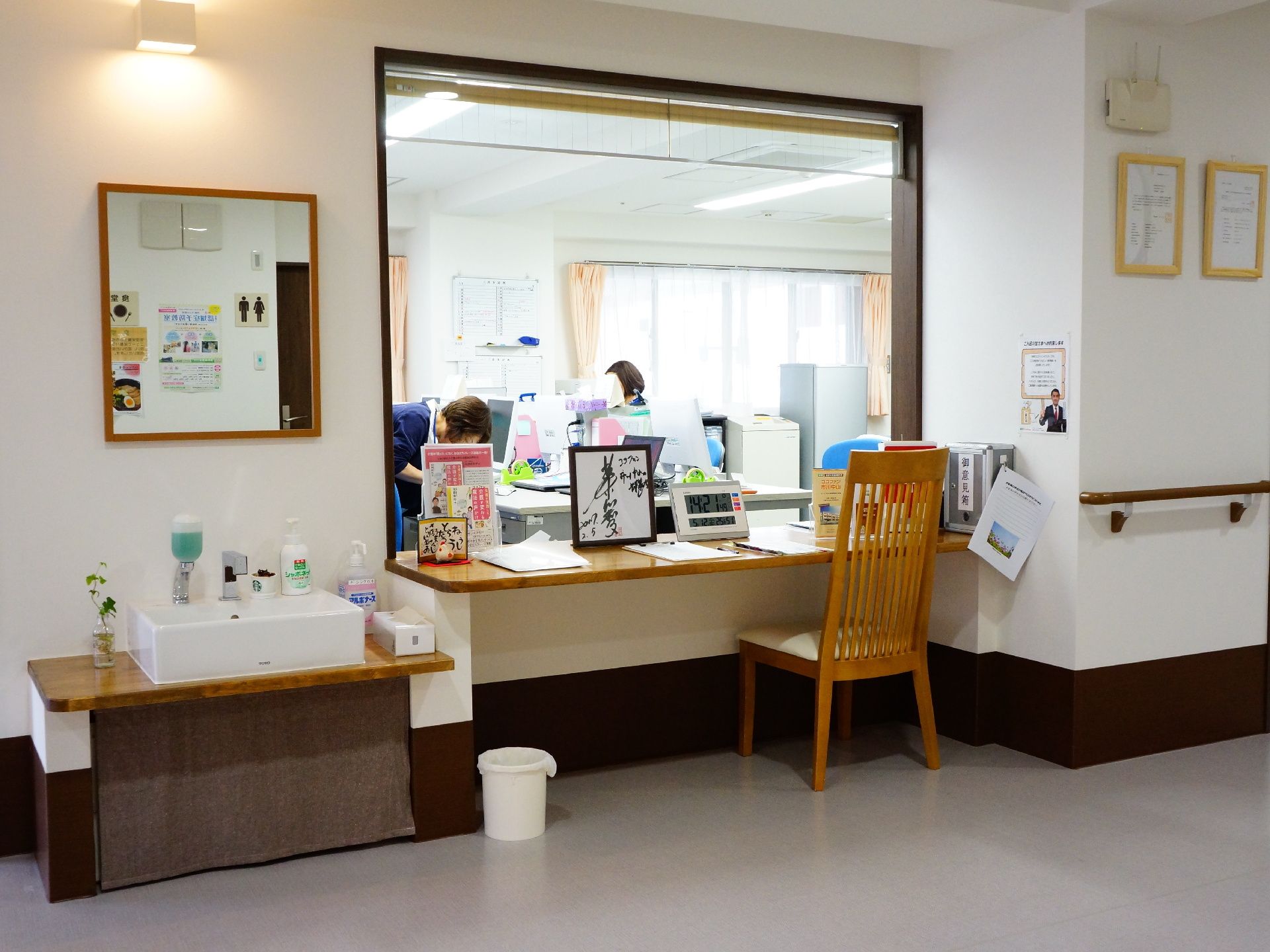 受付カウンターデスクの奥は事務室になっている。横には低い位置に洗面台や鏡が設置してあり、壁に額が掛けてある。