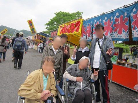 屋台が立ち並ぶ広い道路で、記念撮影をする車椅子の女性2人と付添4人