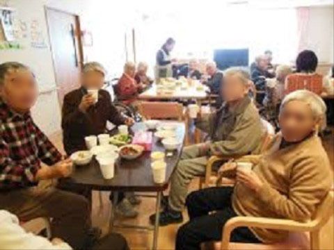 食べ物や飲み物が並んだテーブルを囲み、こちらを向いている高齢者4人