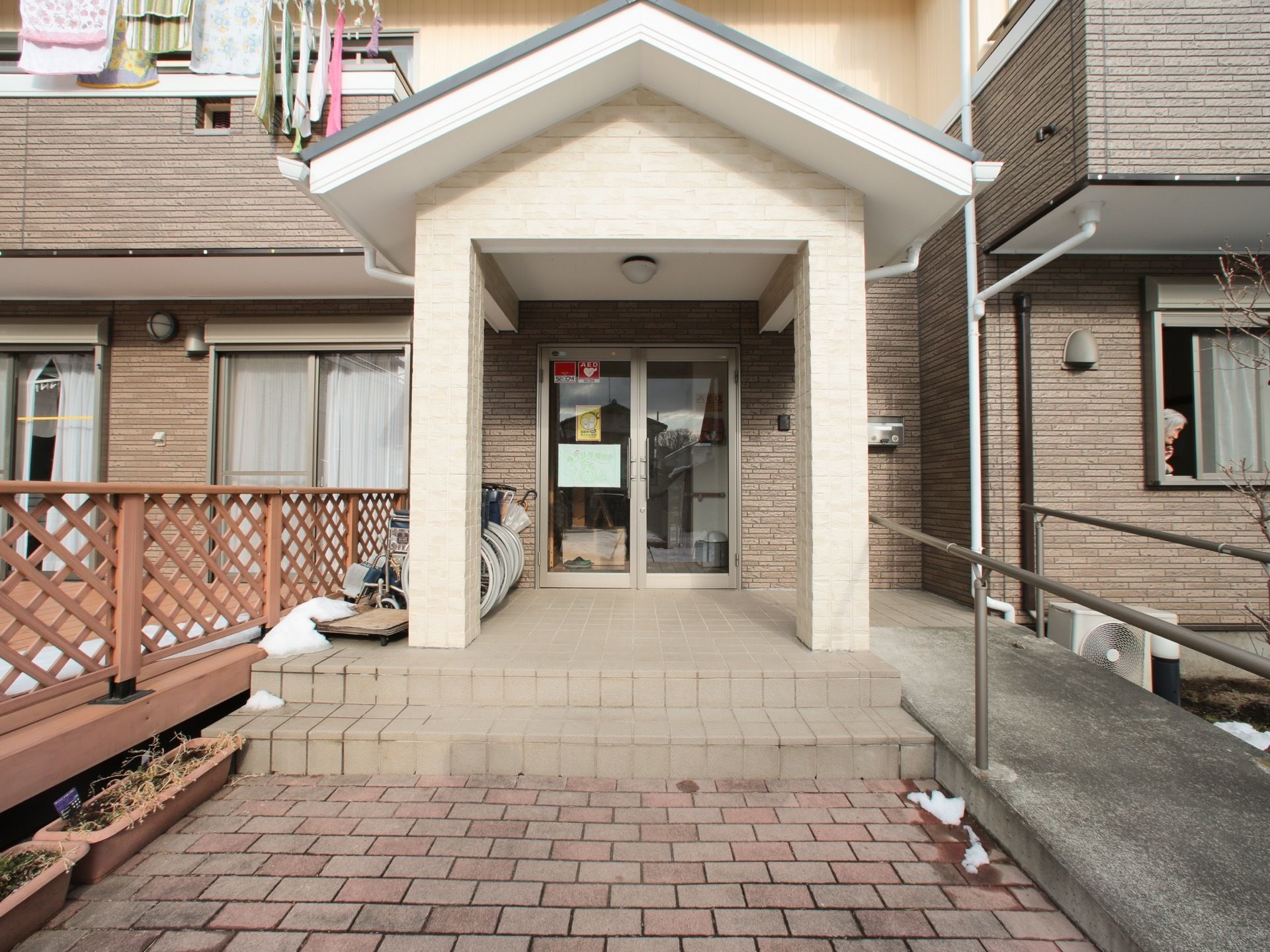 施設の玄関はガラス張りで見通しが良い。前面にはタイル敷きのステップを設け、右側にはスロープを設置している。
