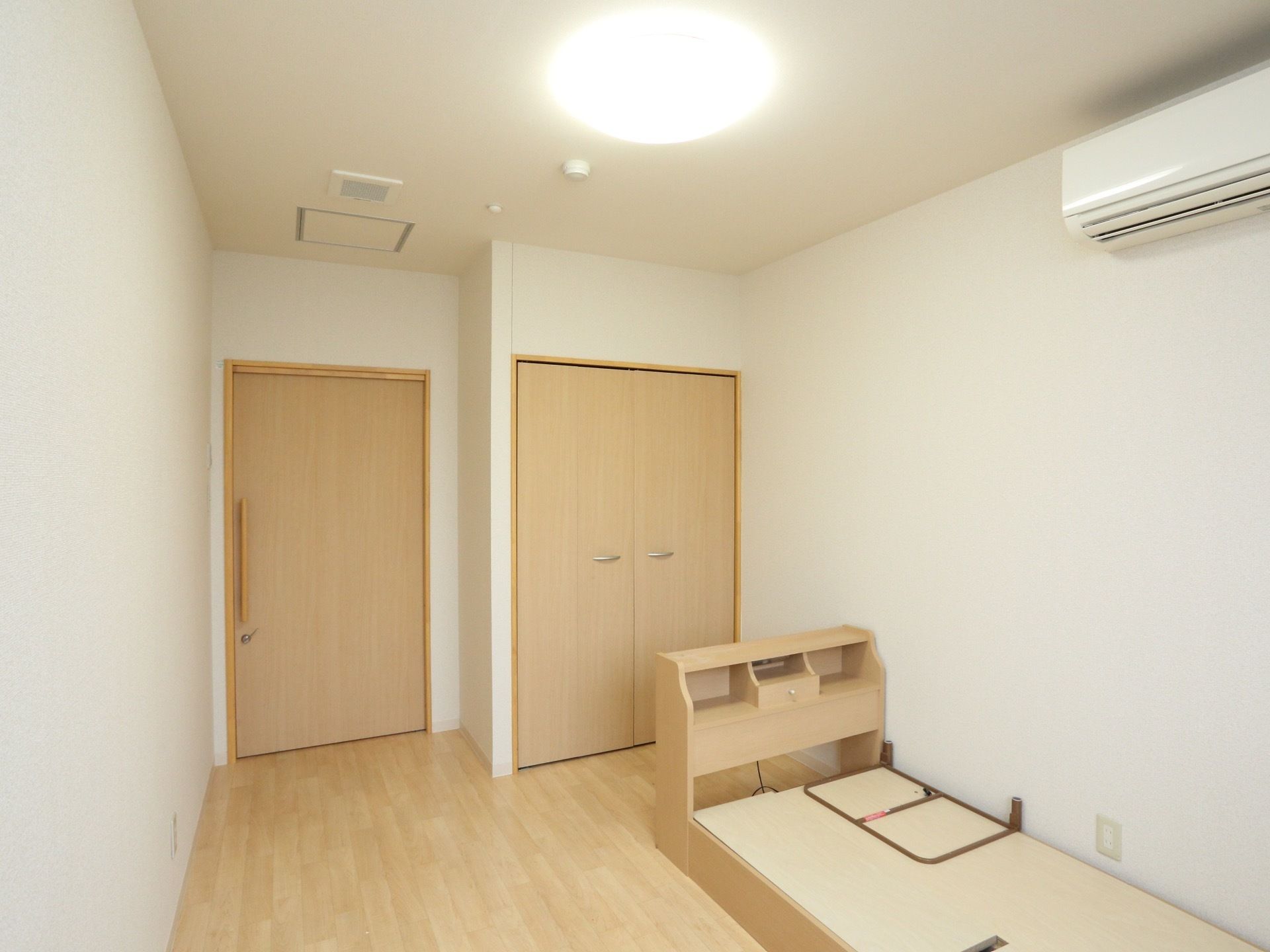 床から少し高さのあるベッドが置かれた居室。それ以外の家具等はなく、フローリングのシンプルな部屋となっている。