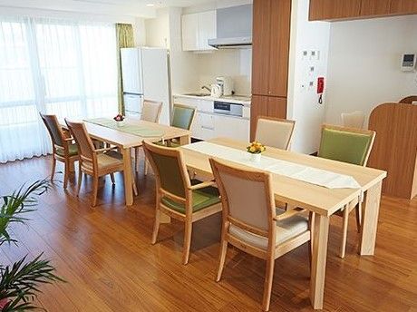 広いキッチンが備え付けられた明るく開放的なリビングである。大きな窓の横には、白い冷蔵庫が置かれている。