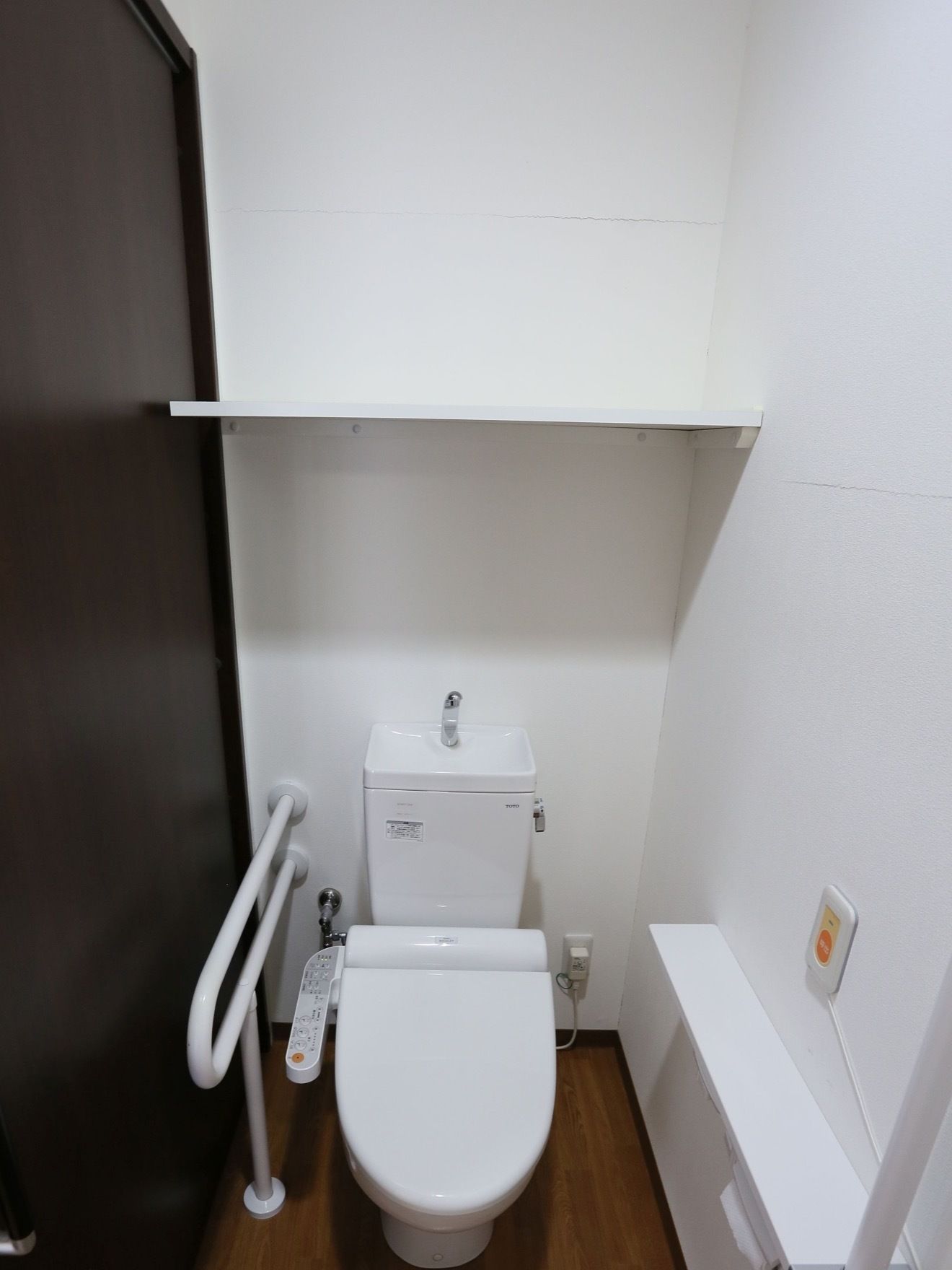 トイレは白を基調とした清潔感のある内装で、便座のそばには手すりが取りつけられている。入口は、ダークブラウンの引戸になっている。