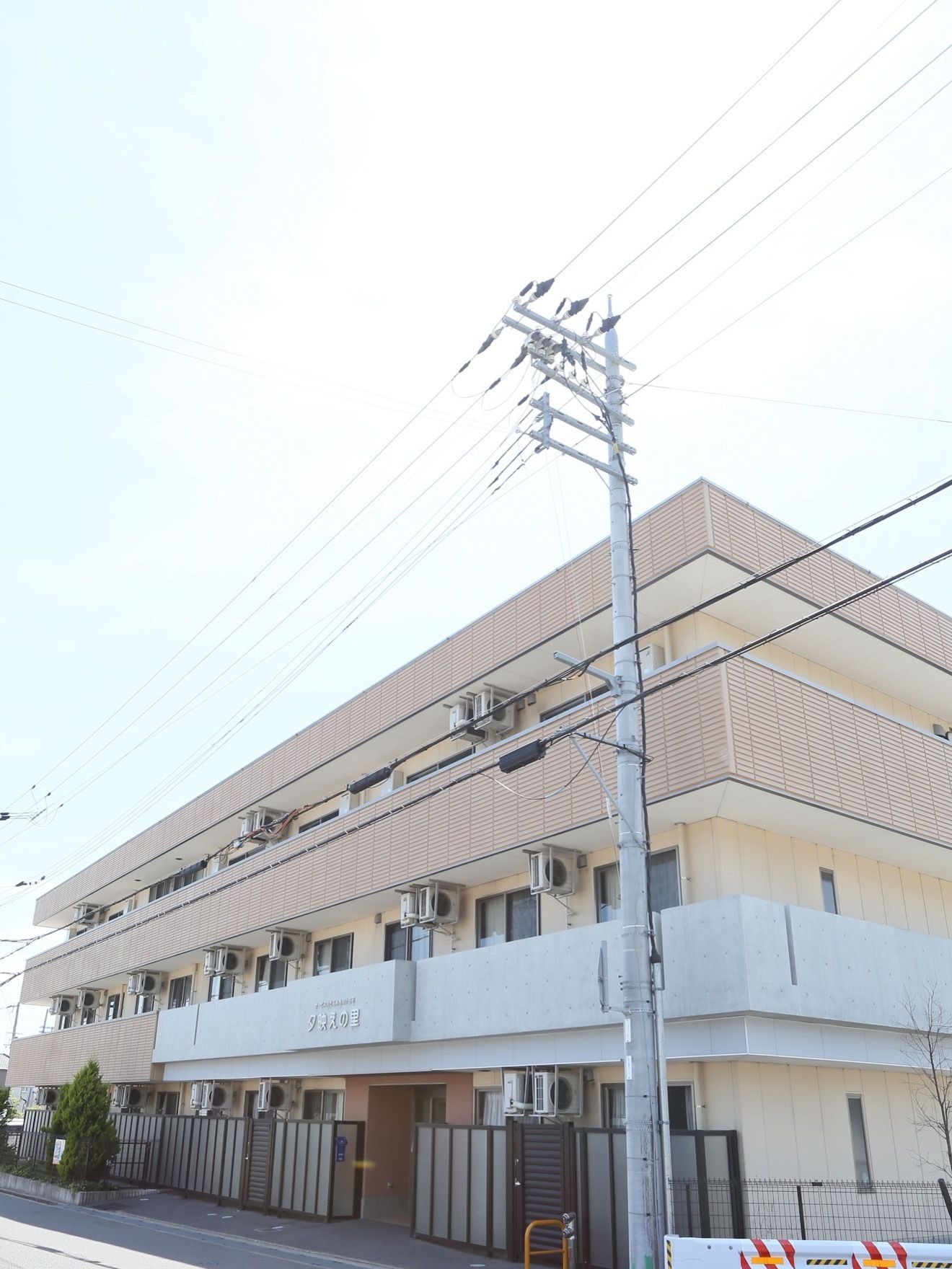 施設は3階建てで、茶色い外壁の建物となっている。1階の居室のある部分には、黒い囲いが設置されている。