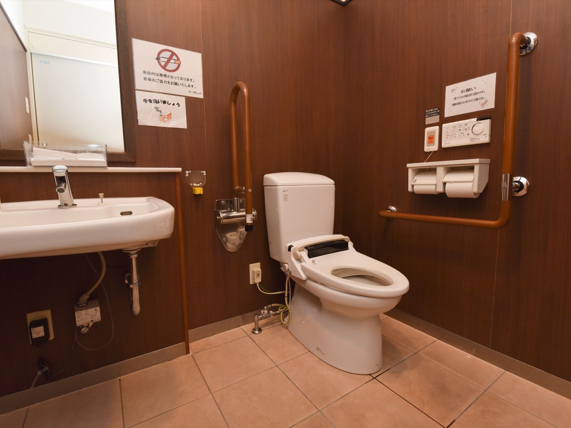 トイレの個室内に、洋式便器と手洗い場が併設されている。便器横の壁に、操作盤や手すり、ナースコールが付いている。