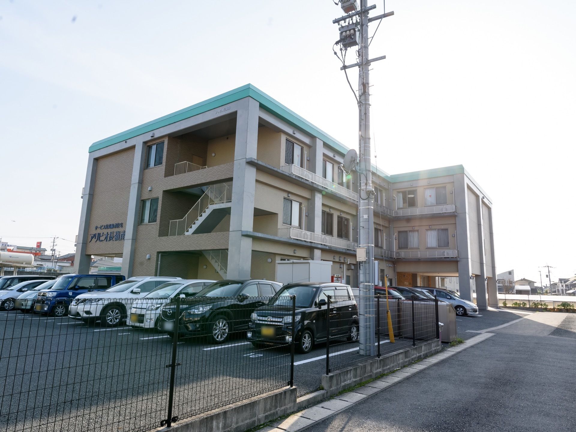 閑静な住宅街の中にあるグループホーム。施設前にはアスファルトで舗装された広い駐車場が設置されている。