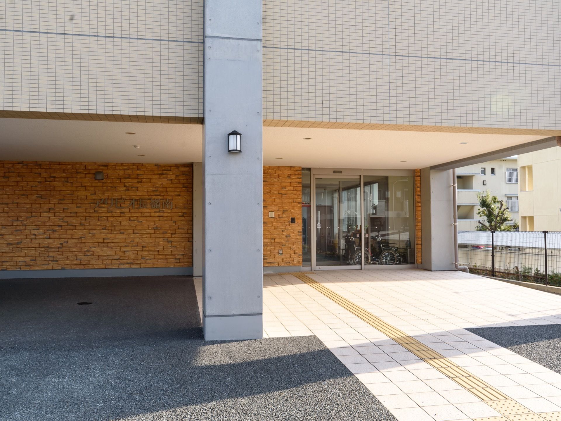エントランス部分には屋根が設置されており、地面には点字ブロックが埋め込まれている。自動ドア横の外壁には、インターホンが設置されている。