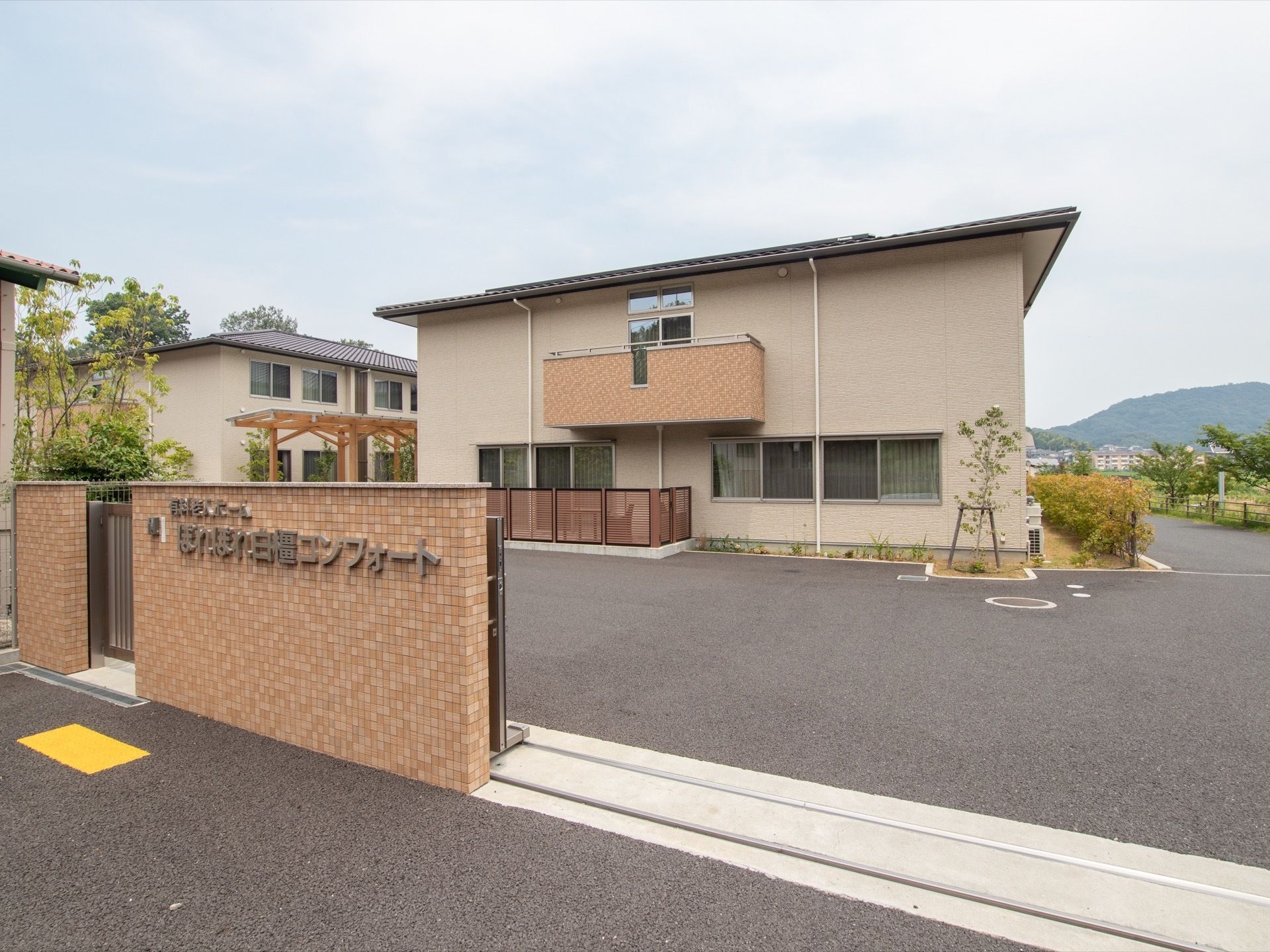 建物の右側には植え込みがあり、きれいに手入れされた緑の木々が並んでいる。その後方には、美しい山並みが見える。