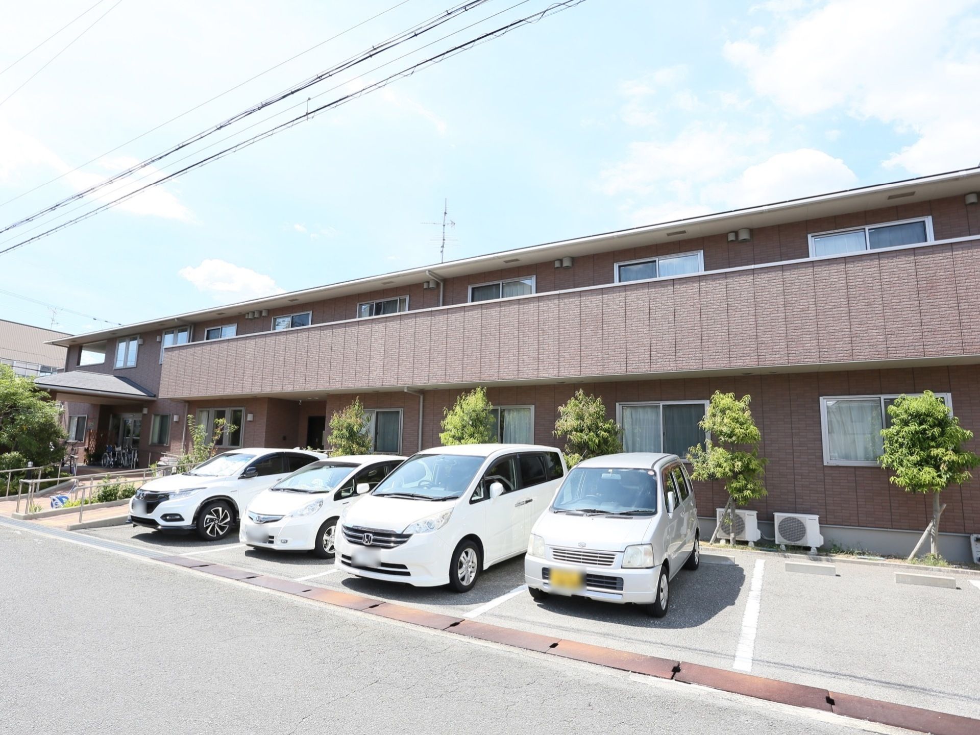 施設はブラウン色の外壁の２階建ての建物である。玄関までの通路には手すり付きのスロープがあり、車椅子をご利用の方も安全に移動することができる。