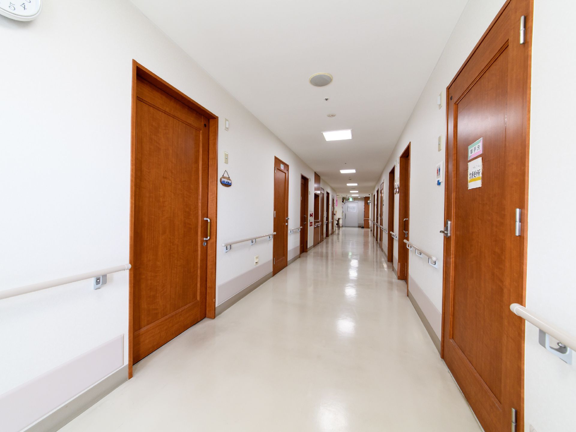 廊下の左右に部屋が設けてある。廊下は段差がないフラットなつくりとなっている。共用のトイレが設けてある。廊下おくにグレイ色の扉が見える。