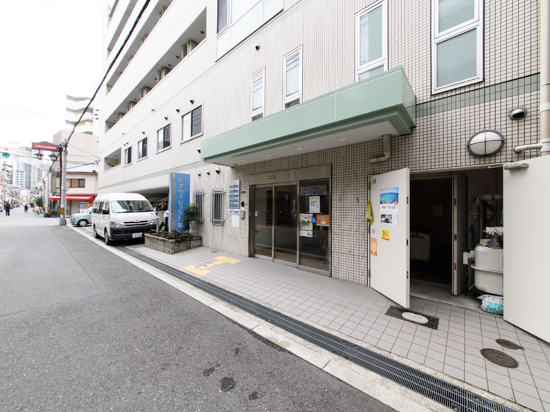 透明な自動ドアが設けられており、段差のないフラットな作りになっている。青い看板が取り付けられている。