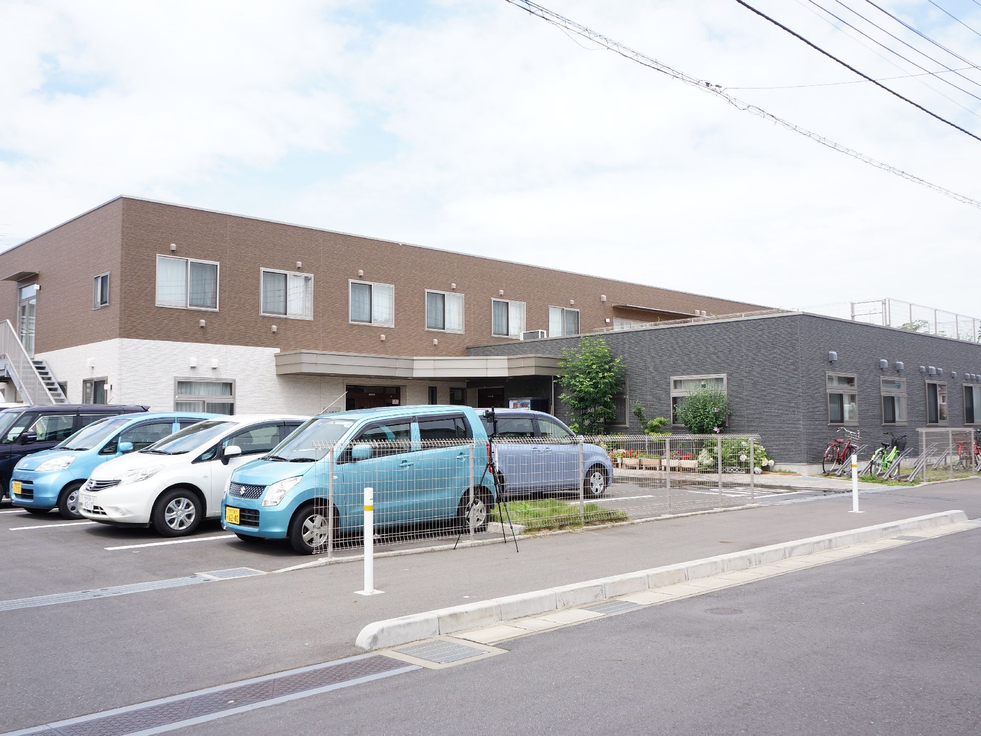 茶色と白色のお洒落な壁の建物は、2階建てで横に広い設計となっている。敷地内には駐車場を完備している。