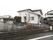 白い２階建ての施設である２階部分には、ベランダが設置されている。駐車スペースが建物前に設けられている。