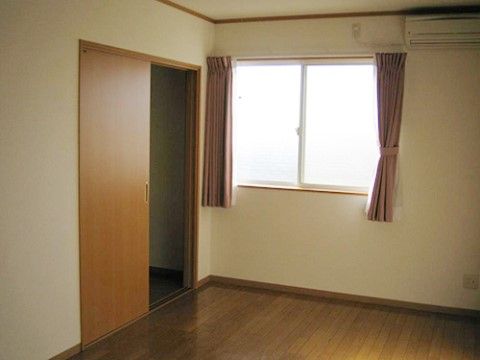 居室内の床は木目調のフローリングで、こげ茶色をしている。壁や天井は白色である。左側にある横開きのドアが開いている。