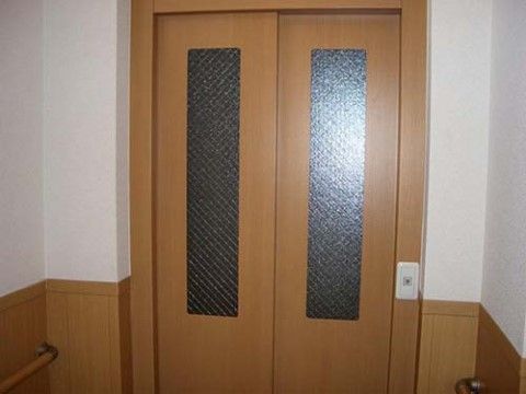 正面にエレベーターの扉がある。エレベーターのドアや壁の下方は木目調で、壁の上方は白色。壁には手すりが設置されている。