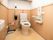 白とベージュが基調の優しい色合いのトイレである。手すりや非常呼び出しブザー、フキン、新聞紙が備わっている。