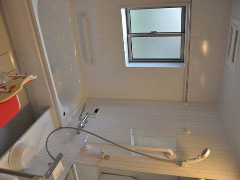 清潔感のある白を基調とした浴室であり、気持ちよくご入浴いただける。手すりや椅子も完備してあり、使いやすい配慮をしている。