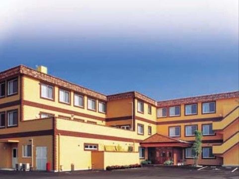グループホーム外観のイメージ図。玄関部分は三角屋根となっており、施設内にアスファルトで舗装された駐車場が設けられている。