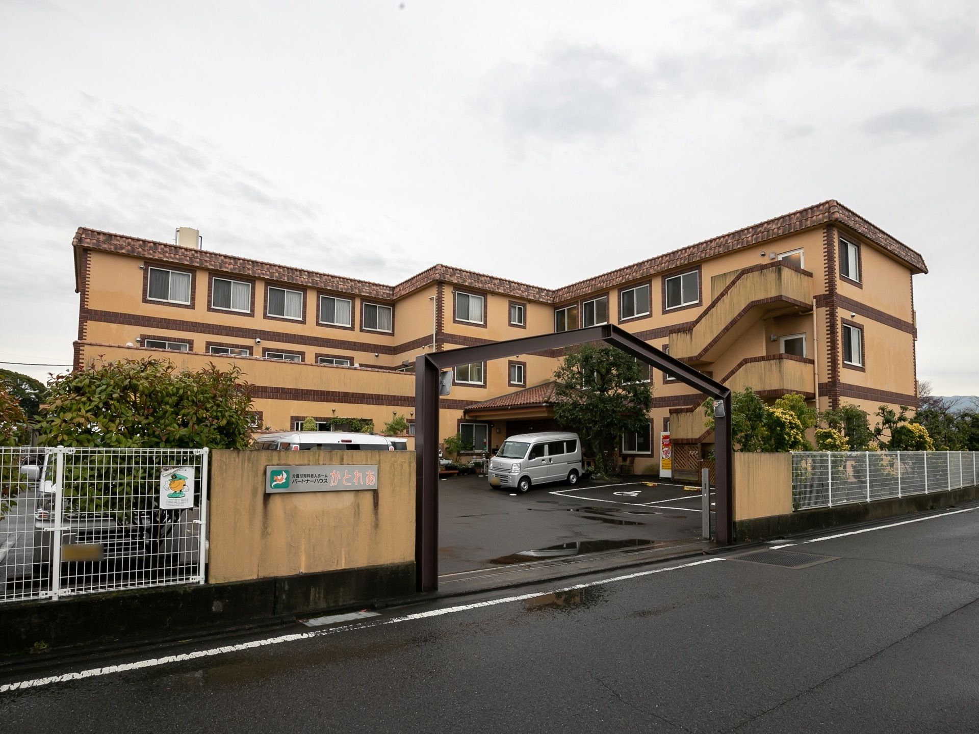 敷地の広い、３階建ての施設の外観である。各居室に大きな窓が備わっているのが見られる。門の脇の壁に施設名が大きく記されている。