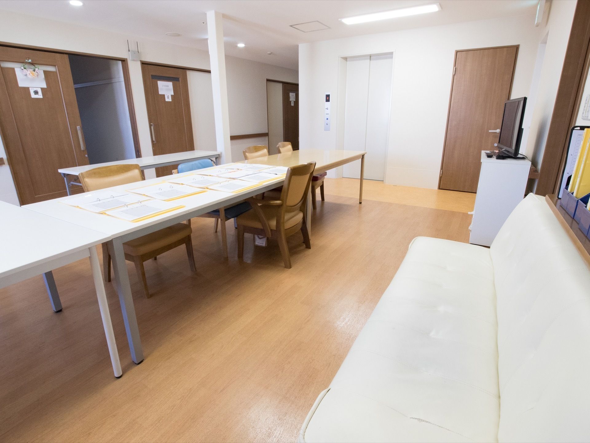 白いテーブルがあり、椅子が３脚置かれている。その奥に木製のテーブルセットもある。壁際にソファが用意されている。