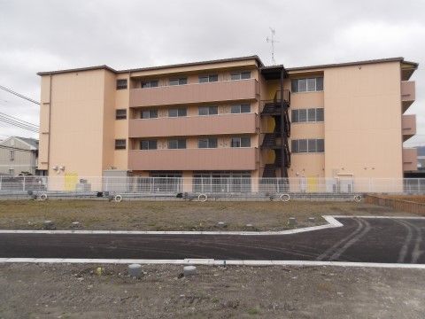 ４階建ての薄いオレンジの建物は、マンションのように直線的で整然とした造りになっている。外階段も設置されている。