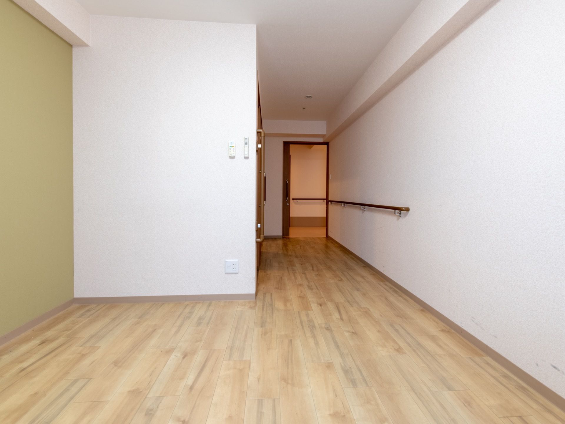 ご入居前の居室の状態で、何も設置されていない。スライド式の居室扉は開かれており、廊下に設置されている手すりが見えている。