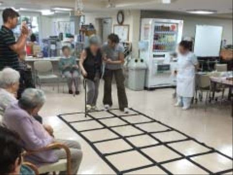 床に敷かれている格子状のスペースを歩こうとしている女性