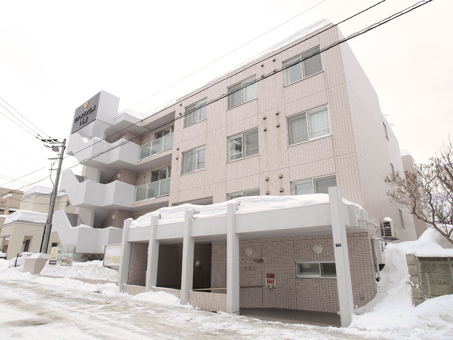建物は4階建てになっていて、道路に面している。左側には外階段がある。外玄関周辺には屋根が付いていて、そばの壁には手すりが付いている。