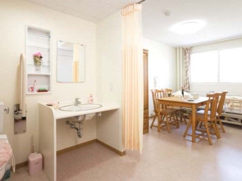 奥にベッドとリビングがあり、手前に洗面台と便器が設置されている居室