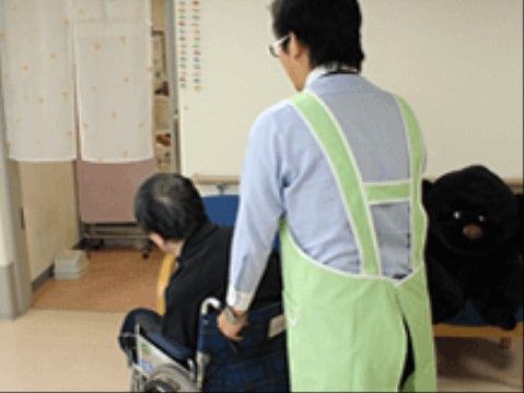 水色のエプロンを着用した男性に車椅子を押されている入居者