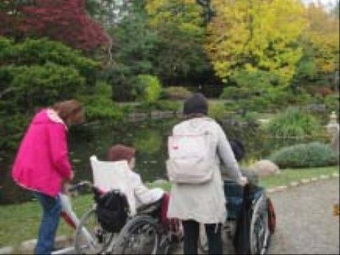 スタッフに付き添われながら、緑豊かな池の脇を散歩する入居者たち