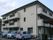 ３階建ての小さなマンション風の外観である。ベランダには洗濯物が干され、駐車場には施設所有の車が置かれている。
