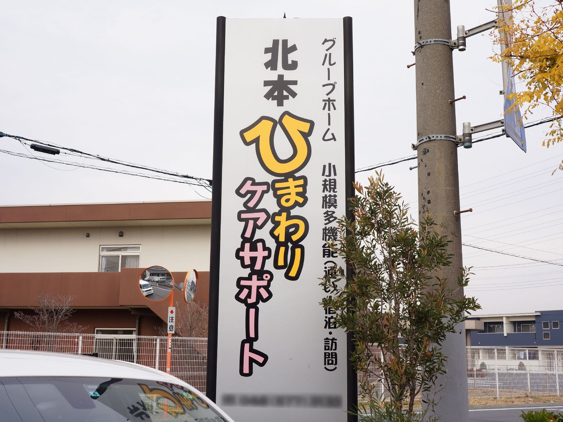 グループホームの入り口には、施設名が書かれた看板を設置している。また看板の横には、木々が植えられている。