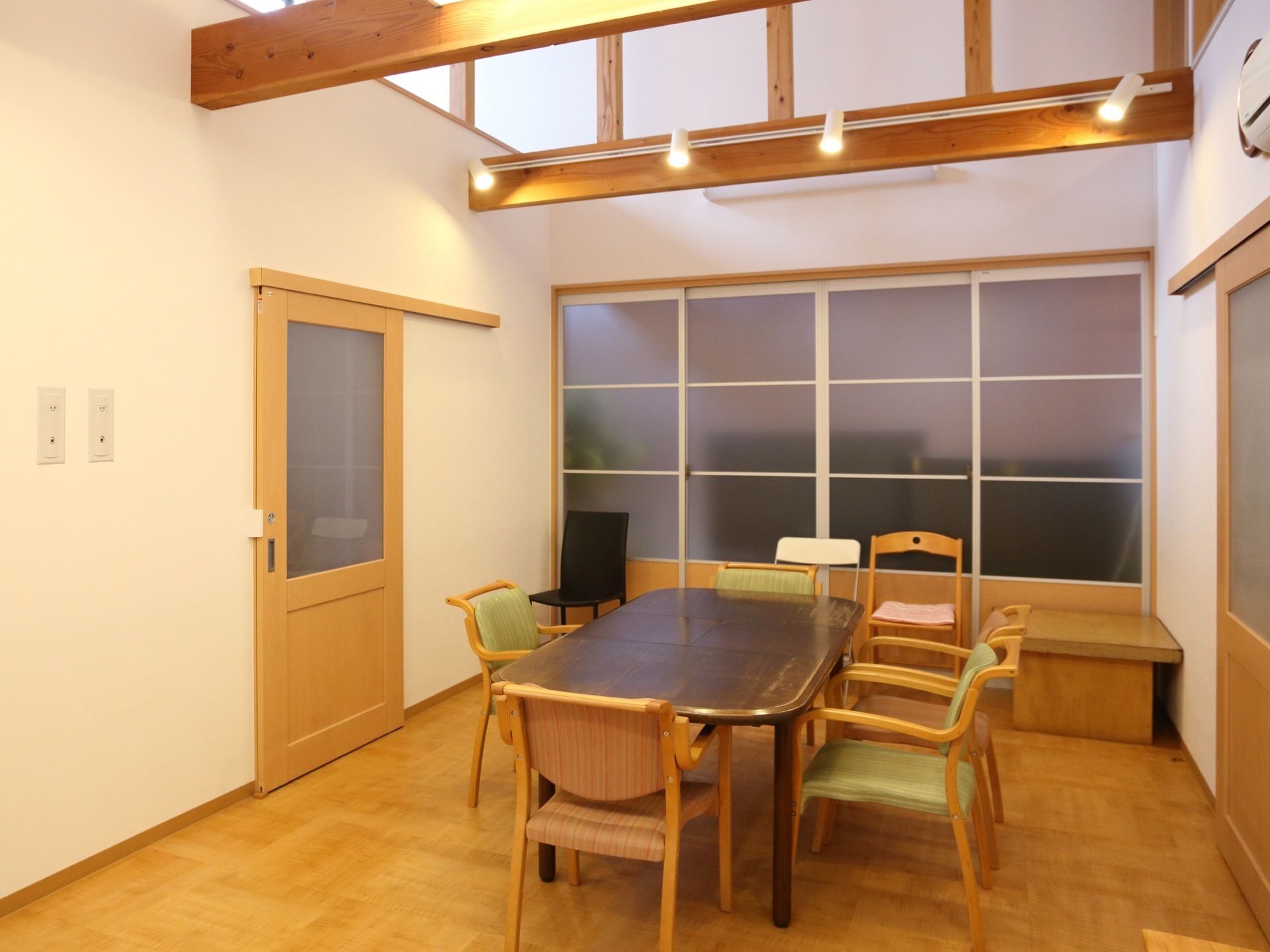 住宅用談話室の中央には、テーブルと5脚の椅子が並べられている。奥の引戸越しにも、椅子が3脚並んでいる。