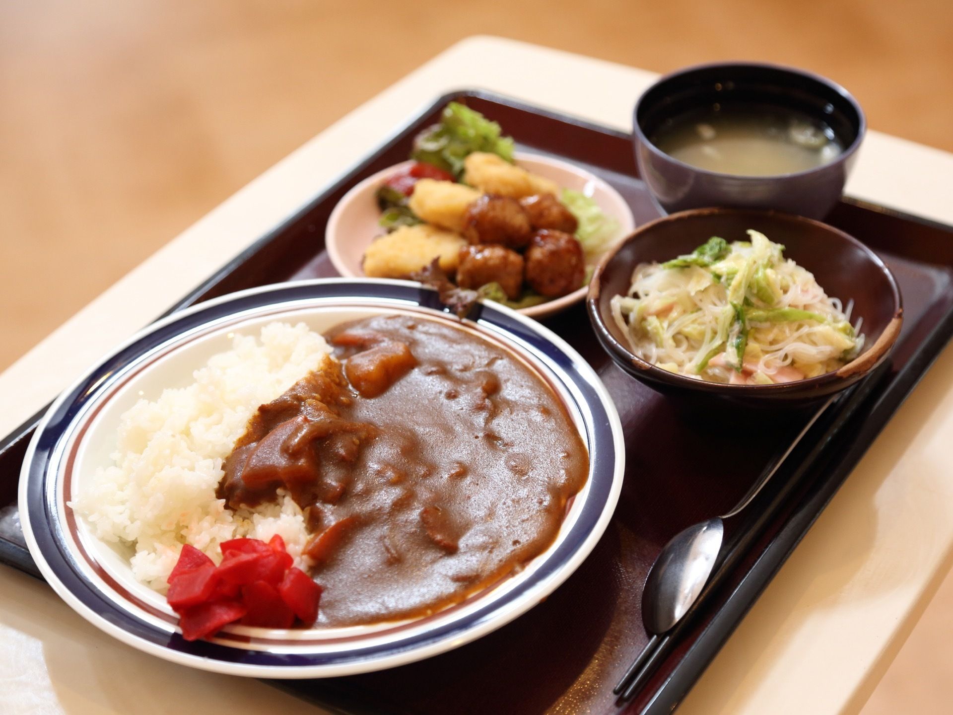 茶色いトレーの上に、食事が並べられている。食事はカレーライスを中心に、サラダやお味噌汁などおいしそうなものが盛られている。