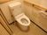 トイレにはタンク付きのトイレが設置されており、奥の壁には横長の手すりが取りつけられている。トイレットペーパー掛けが2つ設けられている。