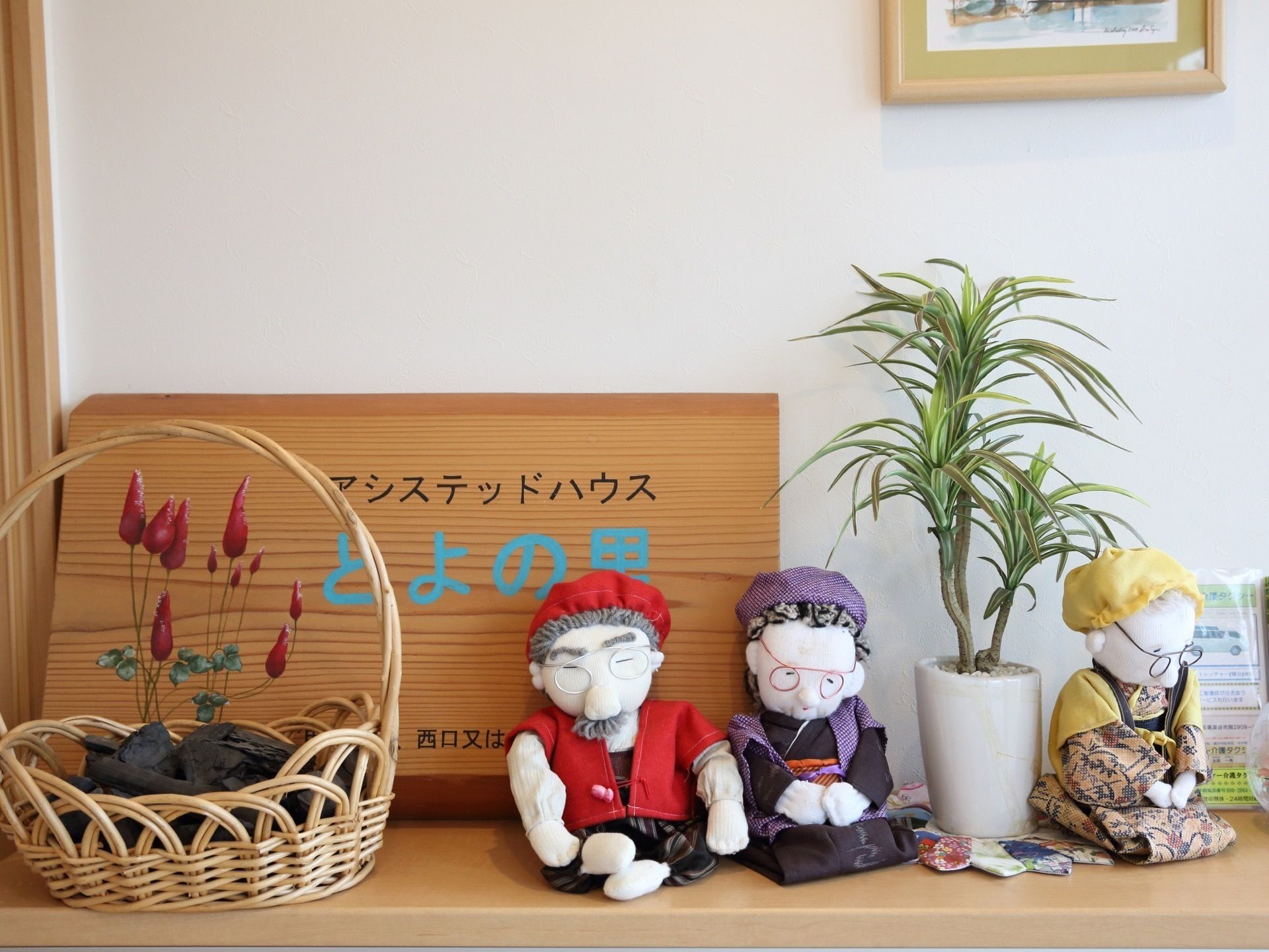 木製の施設看板と、手作りの人形や観葉植物が飾られている棚