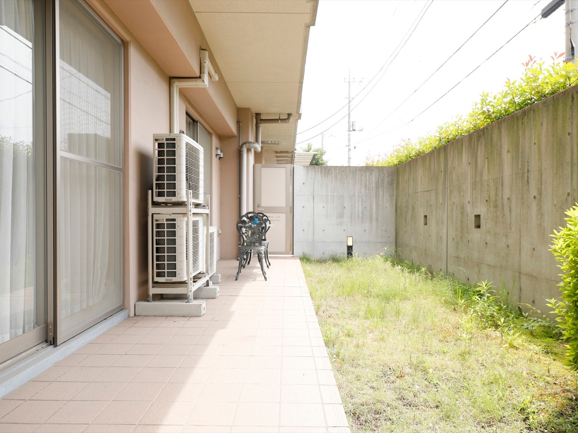 掃き出し窓からタイル敷きのテラスへと続いており、アンティーク風のテーブルと椅子が設置されている。テラスの横には庭がある。