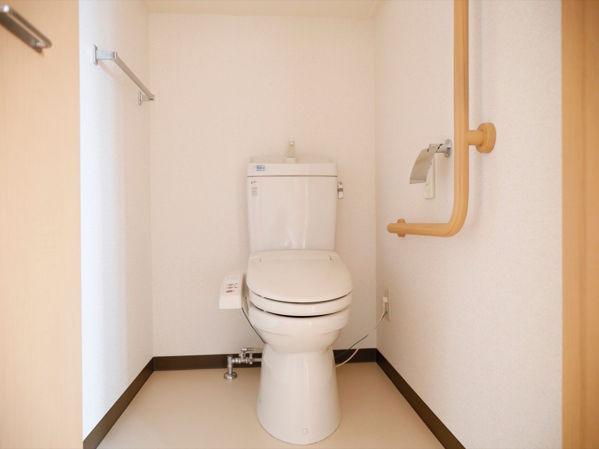 トイレは白で統一されており、清潔感あふれるスペースとなっている。木の温かみのあるＬ型の手すりが設置されている。