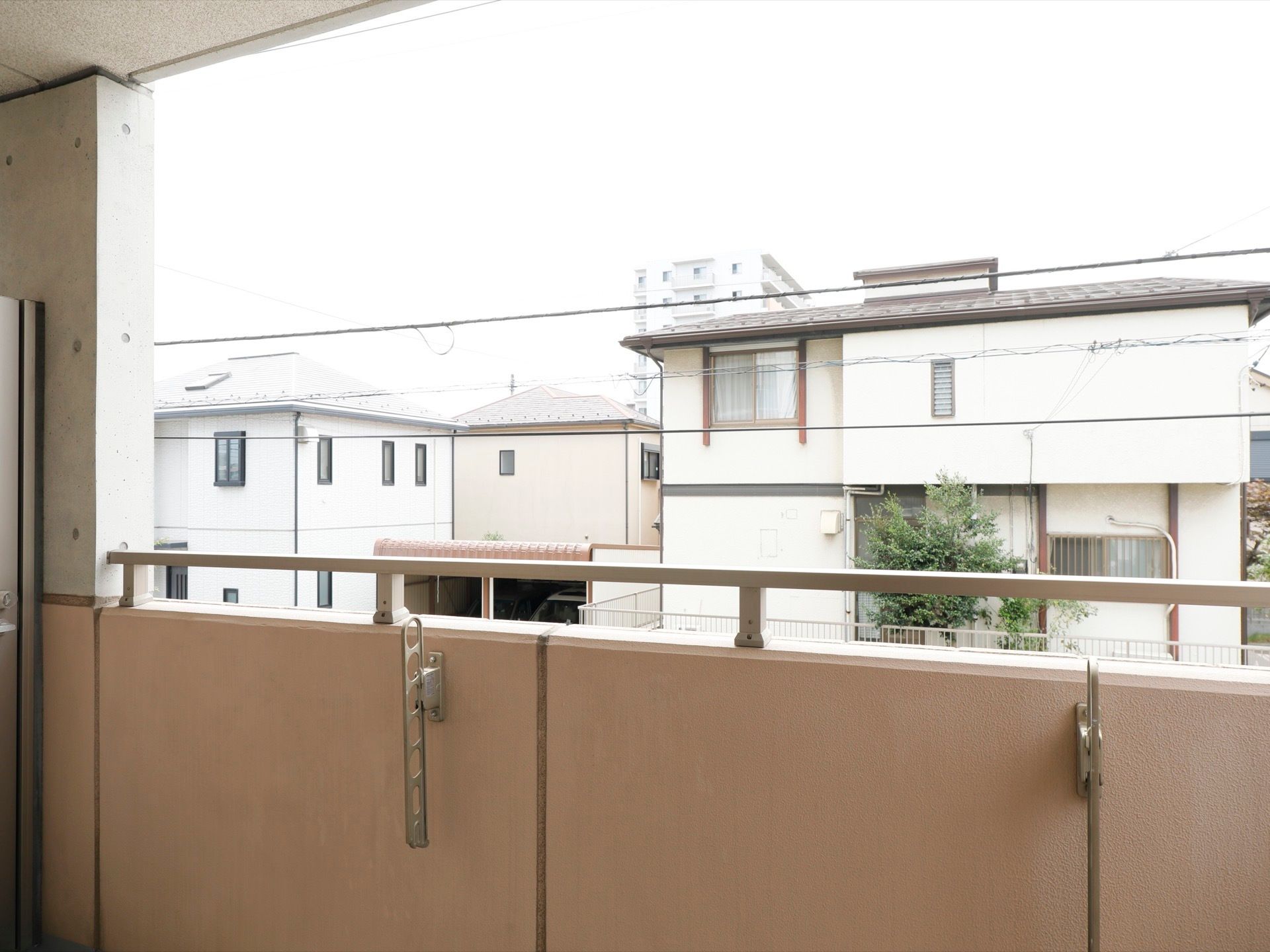 居室にベランダがあり、腰壁には物干し用の金具と手すりが取り付けられている。近隣の住宅が立ち並んでいるのが見える。