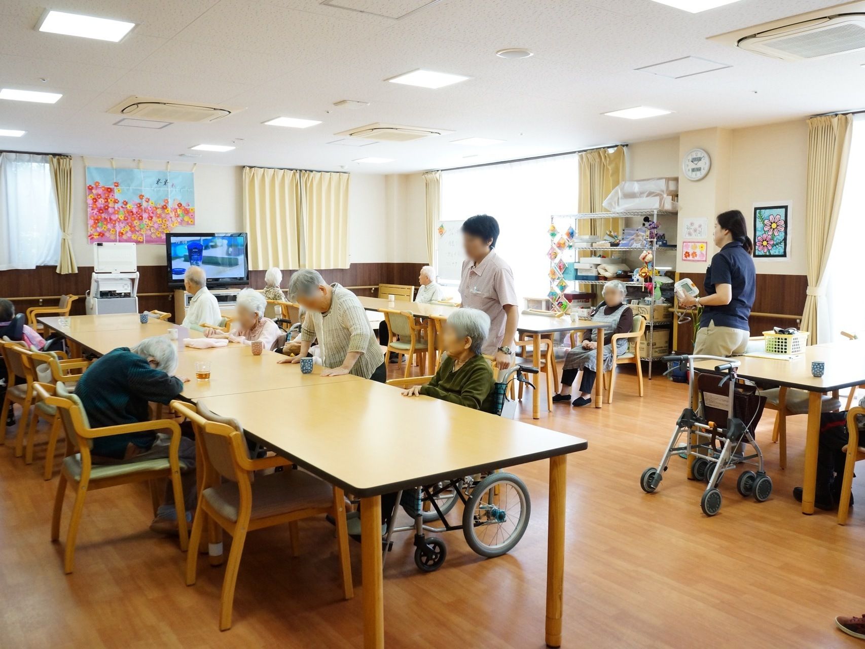 食堂は窓が多く光が差し込んでいる。テレビの近くの壁には、オレンジや黄色の鮮やかな花の飾りが付けられている。